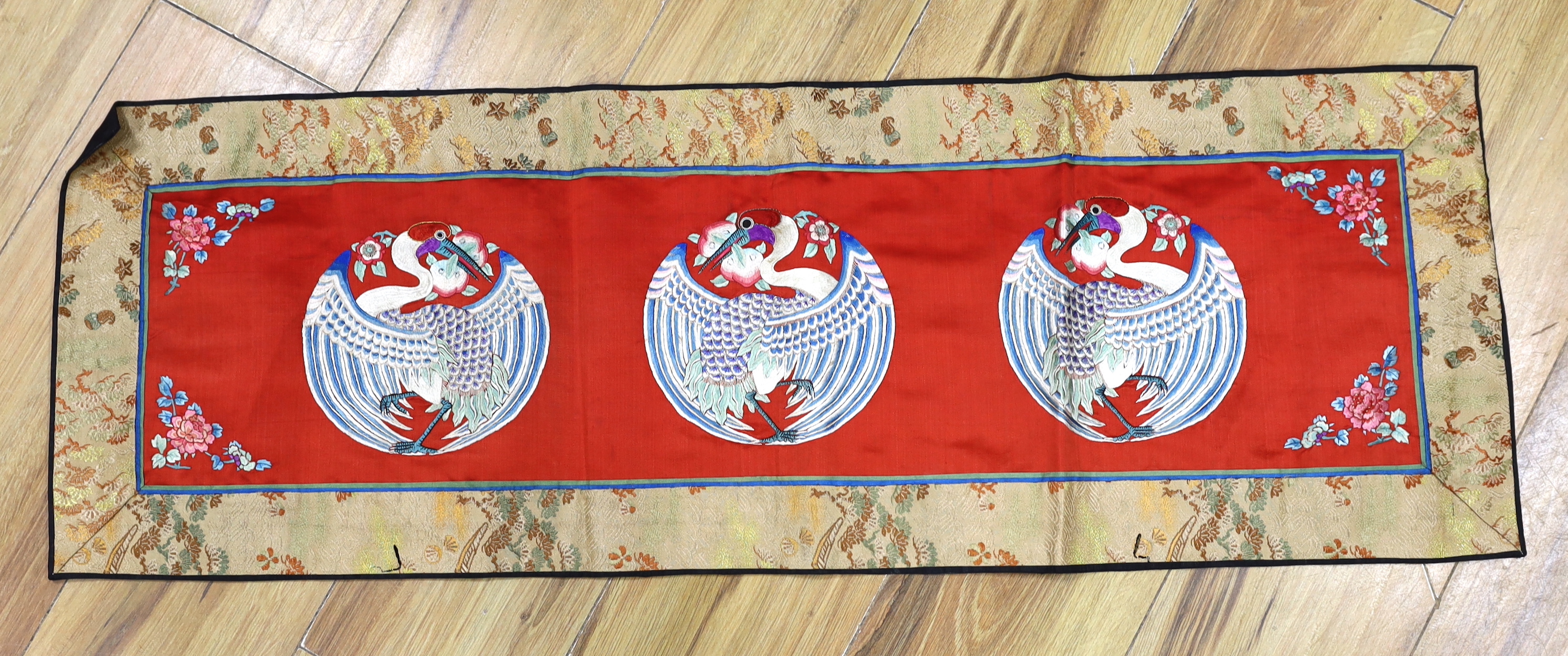 A long Chinese silk embroidered runner embroidered with the figure of Fu and boys, symbolic peaches, phoenix and flowers, possibly an altar cloth together with two other smaller runners, largest runner 202cm long x 55cm